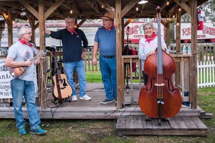 Outdoor band performance with four musicians and instruments under a wooden gazebo.