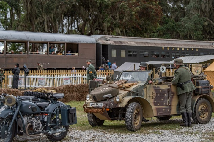 A german car and motorcycle parked in front of a train