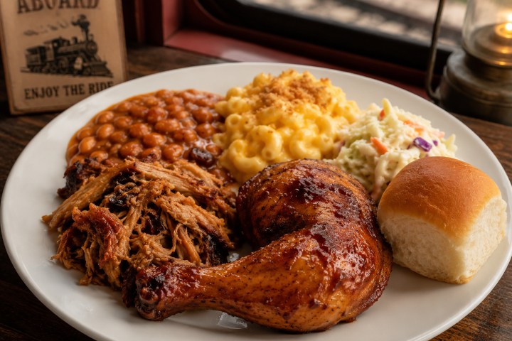 Plate with grilled chicken, pulled pork, baked beans, mac and cheese, coleslaw, and a roll.